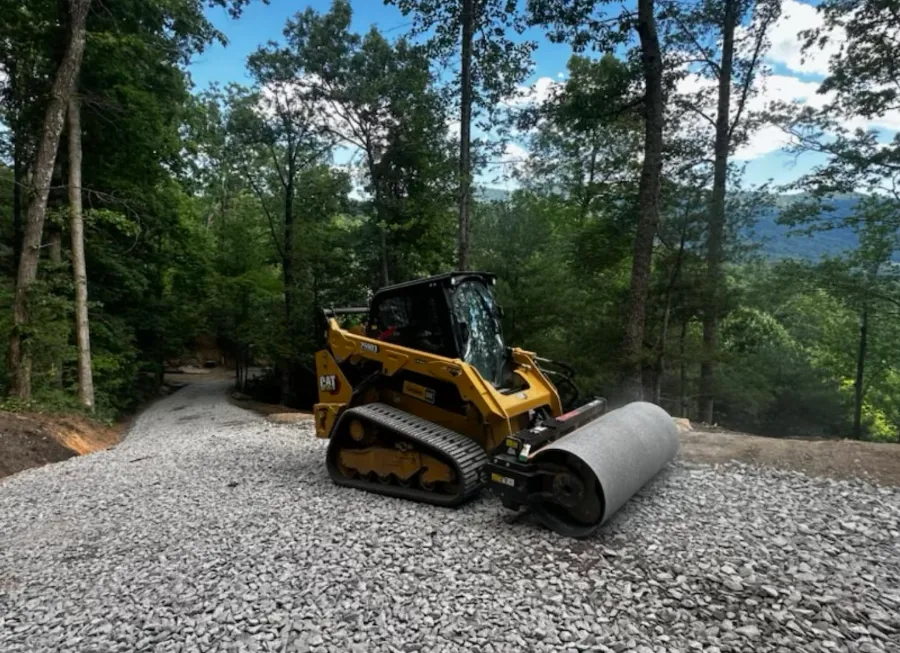 Track loader with a roller compacting a gravel drive